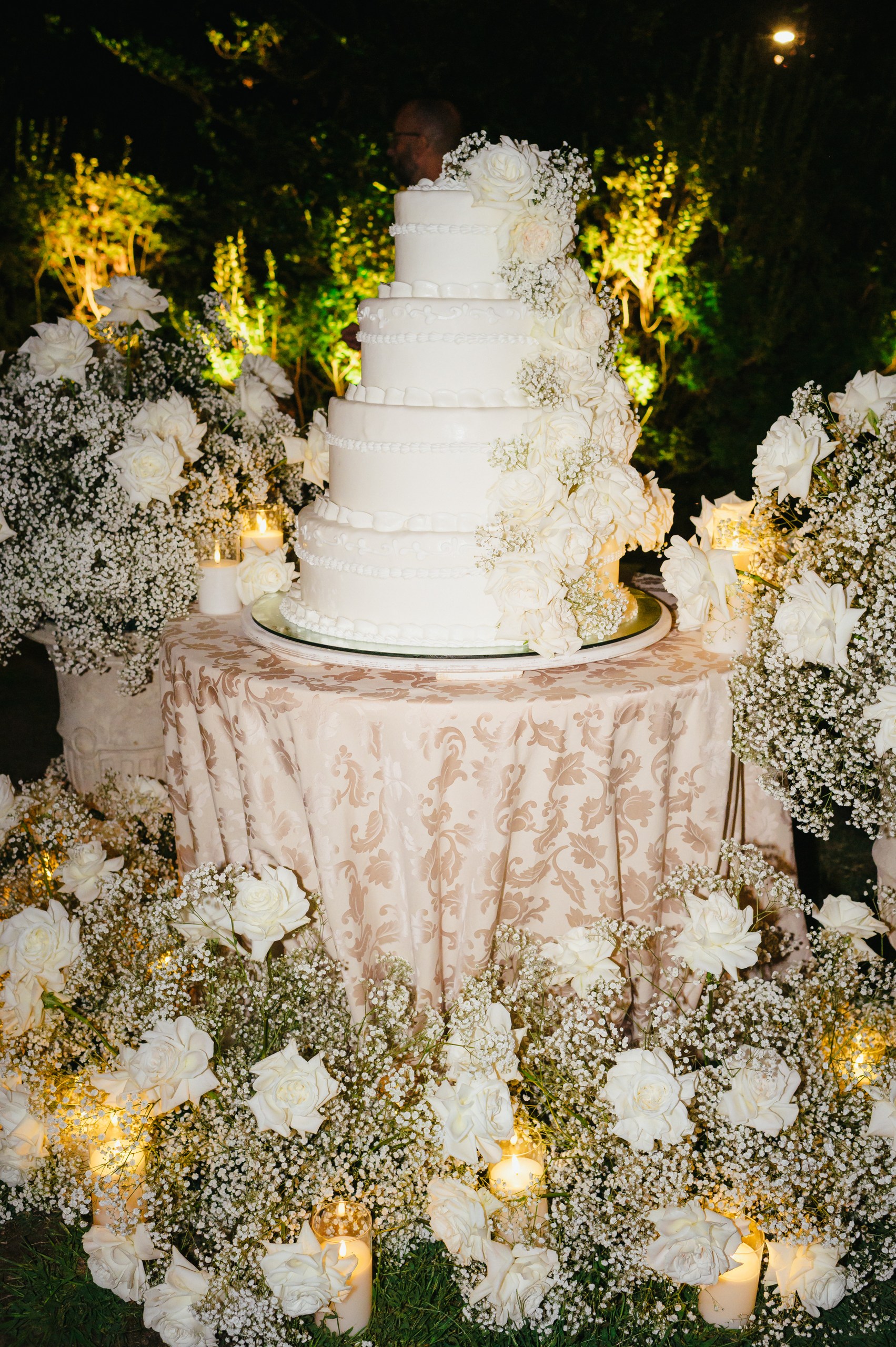 Luxury Wedding Cake – Lake Maggiore Elegant white tiered wedding cake surrounded by white roses, baby's breath and candles at a Lake Maggiore wedding.