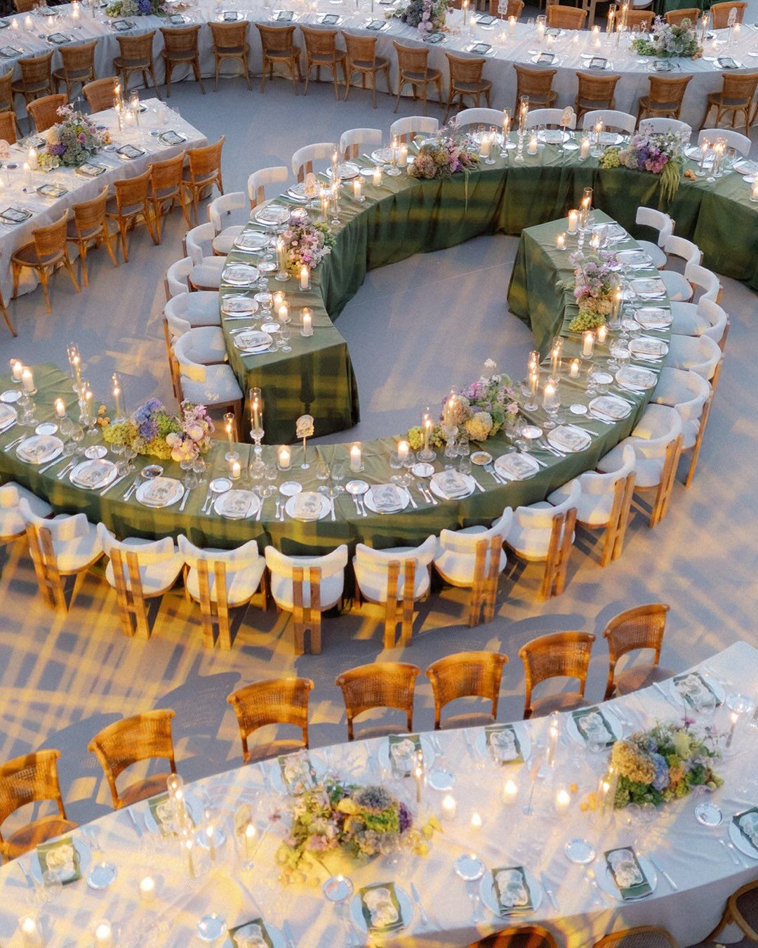 Elegant curved wedding reception table with floral centrepieces, white table settings and wooden chairs in an outdoor setting