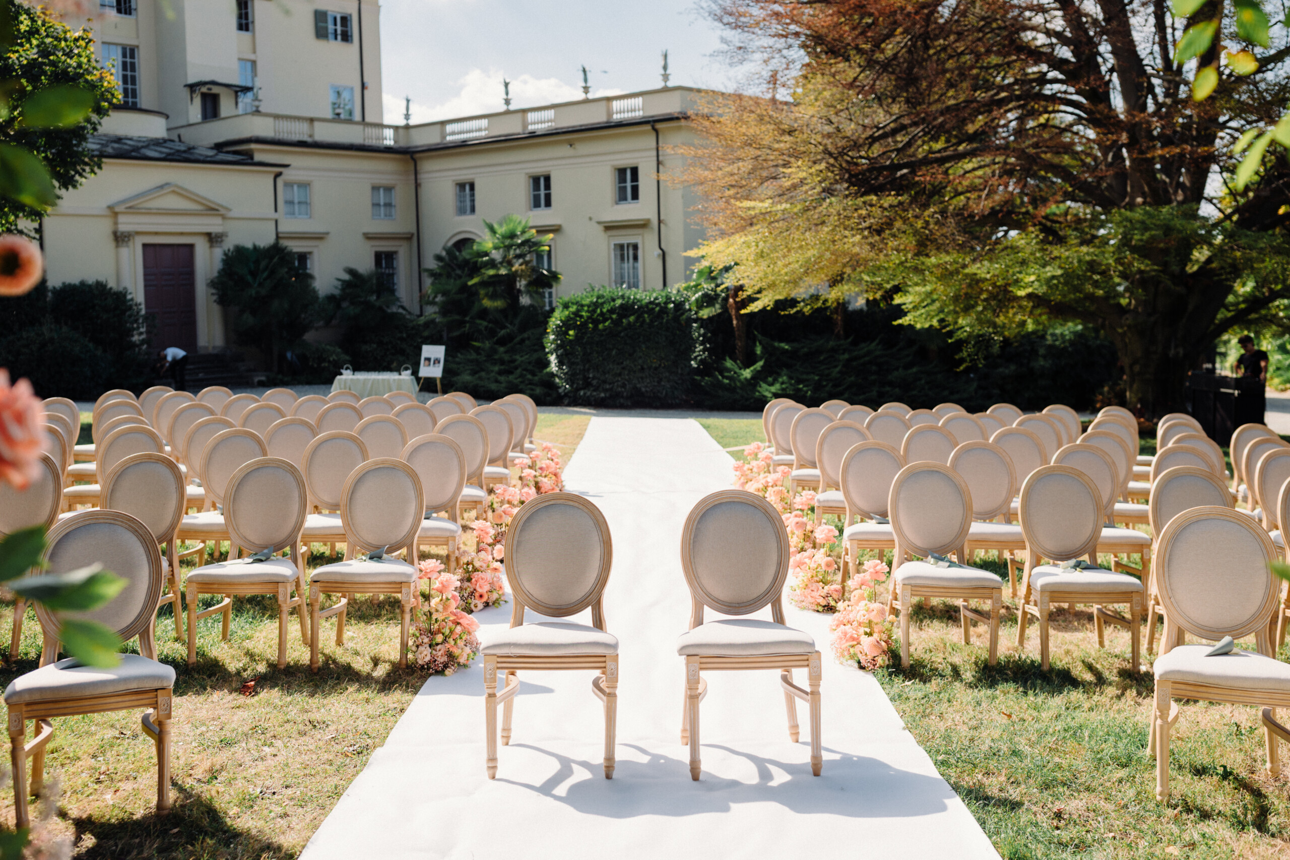 Wedding Ceremony Seating – Villa Cimena Wedding Bride and groom's chairs at the end of a white wedding aisle decorated with pink flowers in the gardens of Villa Cimena.