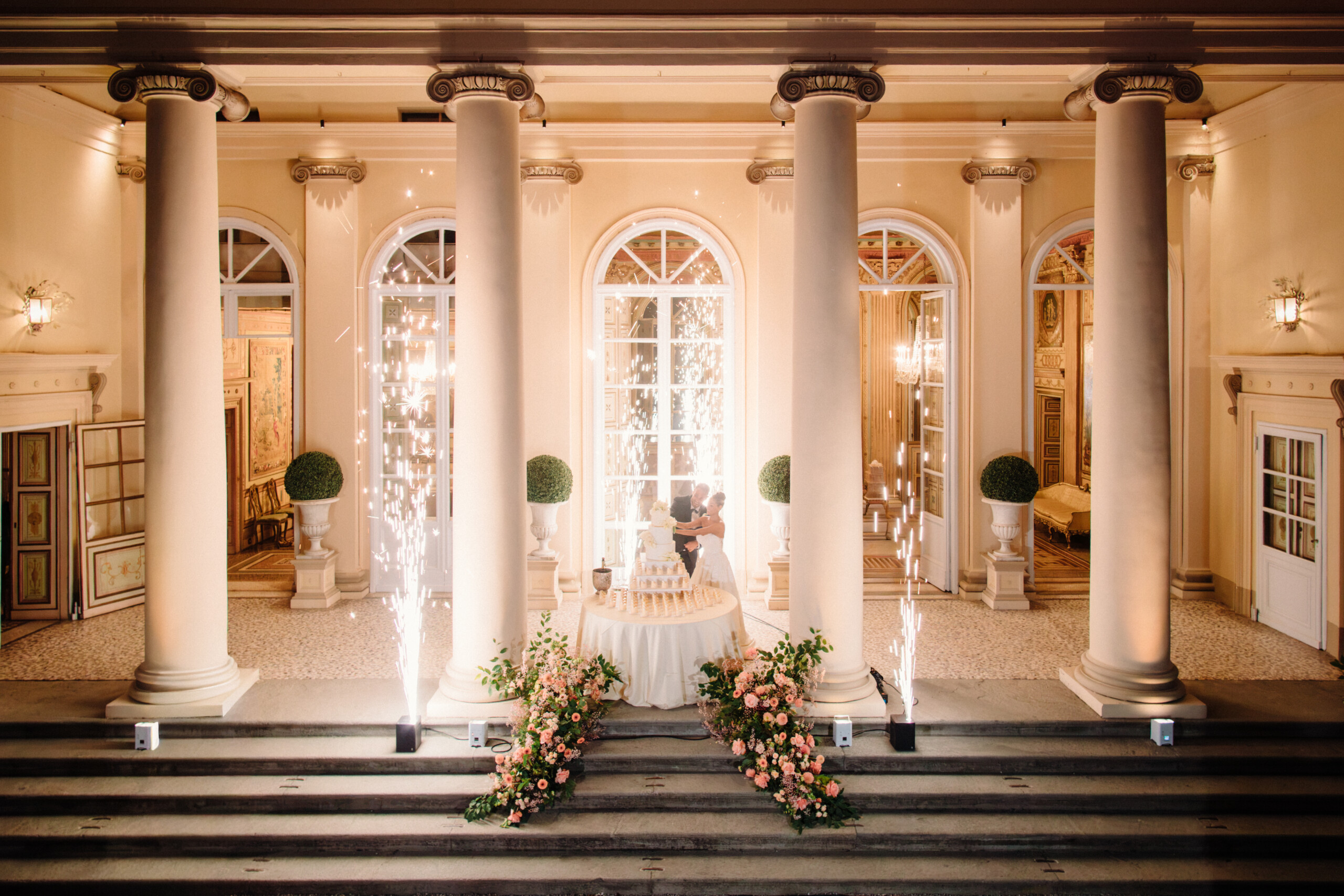 Wedding Cake Display at Villa Cimena in Turin Wedding cake decorated with flowers and sparkling fountains in front of the historic facade of Villa Cimena.