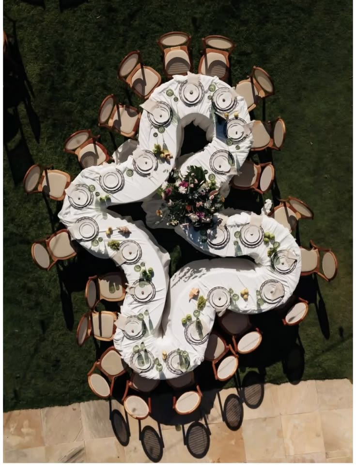 Aerial view of a serpentine wedding reception table decorated with flowers and candles in an elegant courtyard.