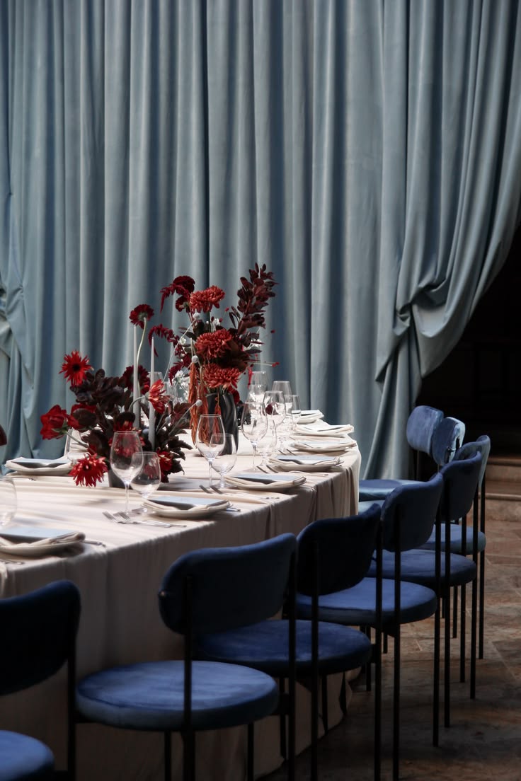 Mise en place matrimonio bordeaux e blu con composizioni floreali rosso intenso, sedie in velluto blu e drappeggi coordinati.